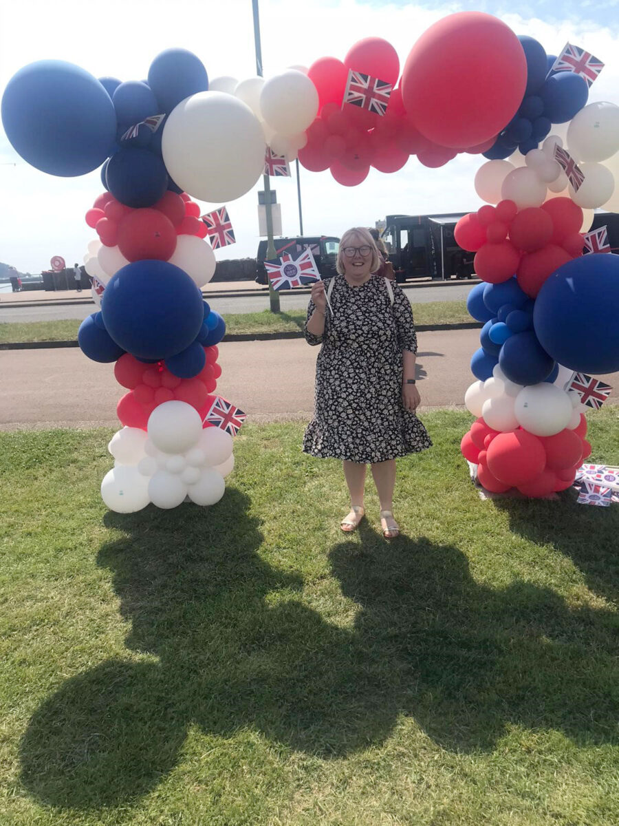 Chantelle standing in a summer dress under an arch of red, white and blue balloons.