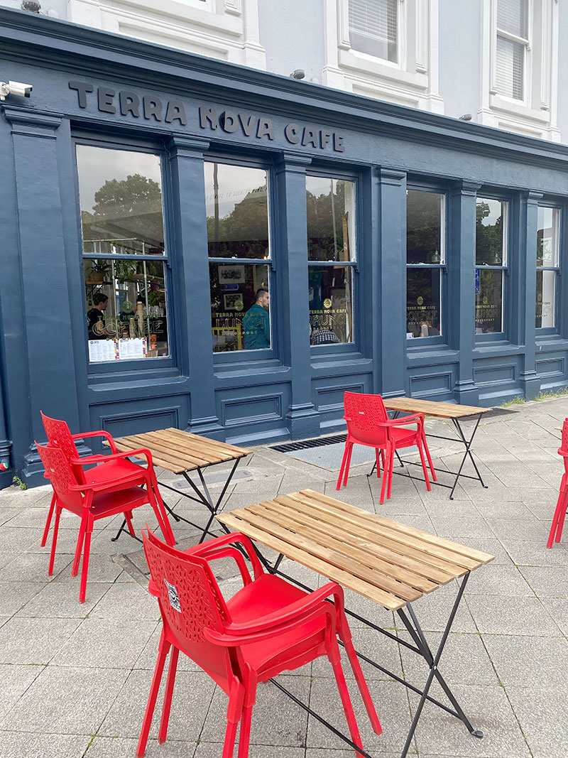 Side view of the Terra Nova cafe with red chairs and wooden tables outside