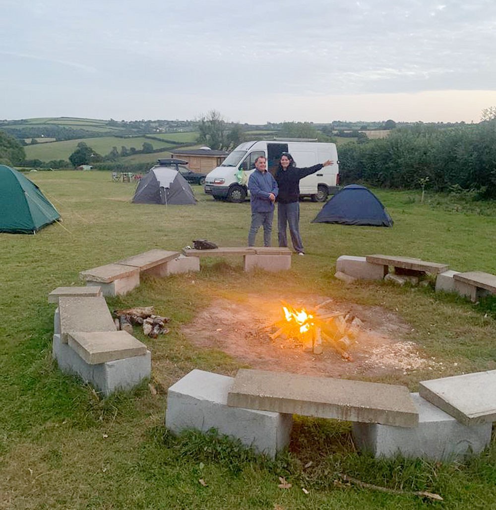 Photo of a camp site with a camp fire inside a circle of stone seats in the foreground.