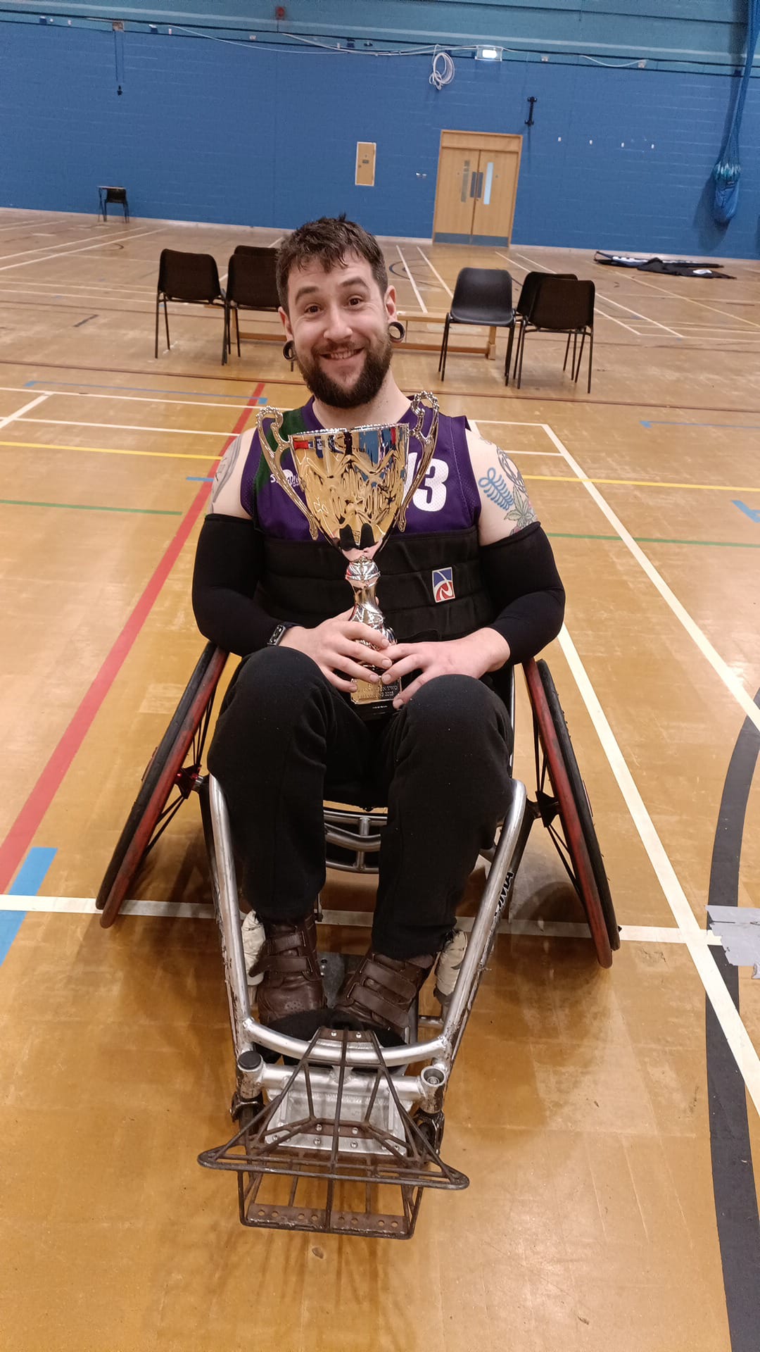 Rich holding the winners cup in his wheelchair in a gym.