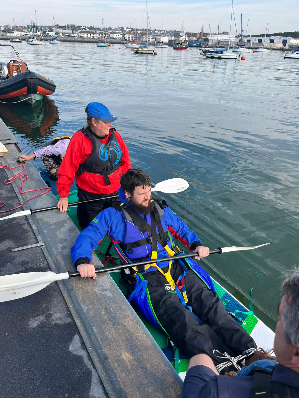 A man is being taught how to kayak on Plymouth Sound with two instructors.