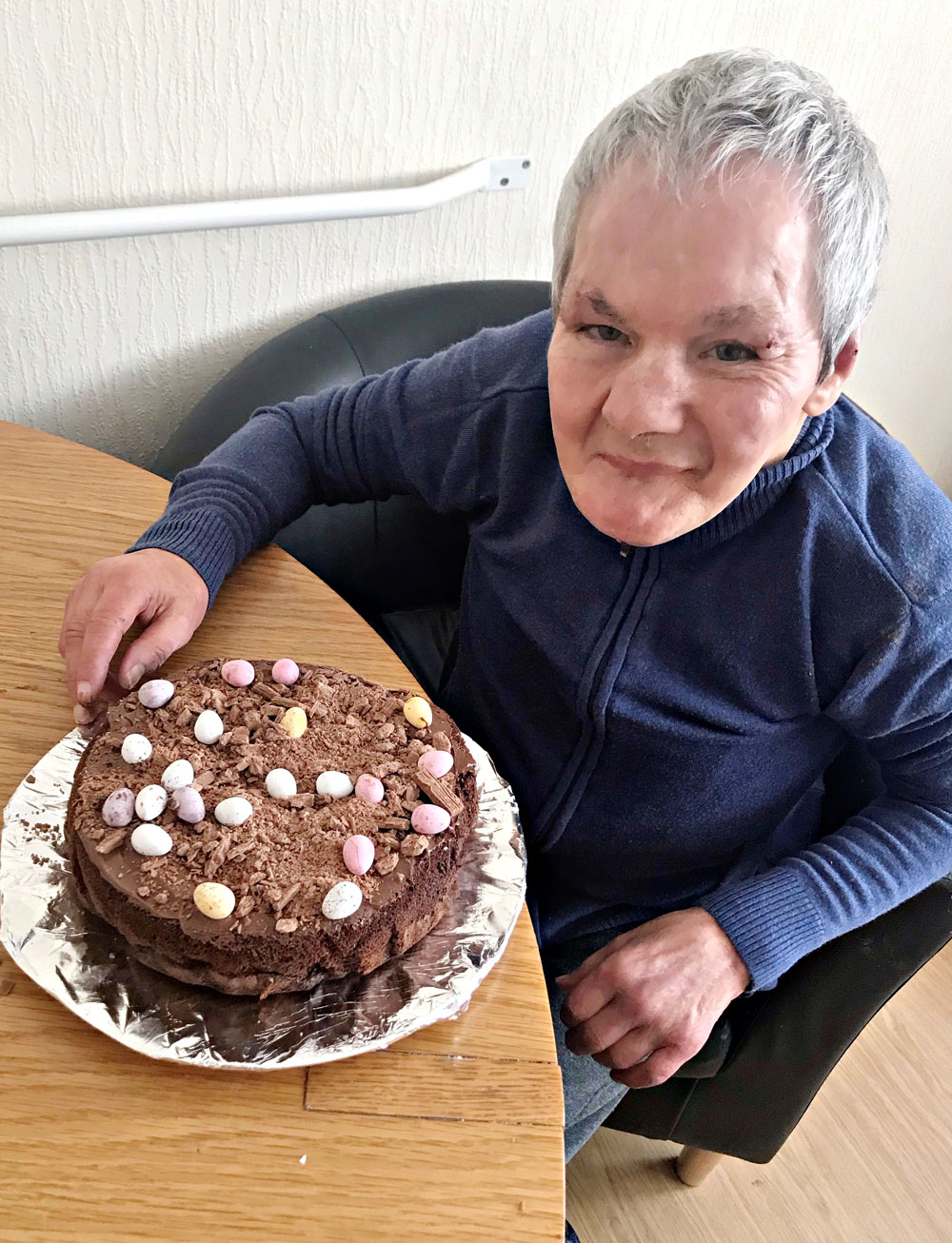 Ian sitting at a table with his finished cake on a silver paper tray.